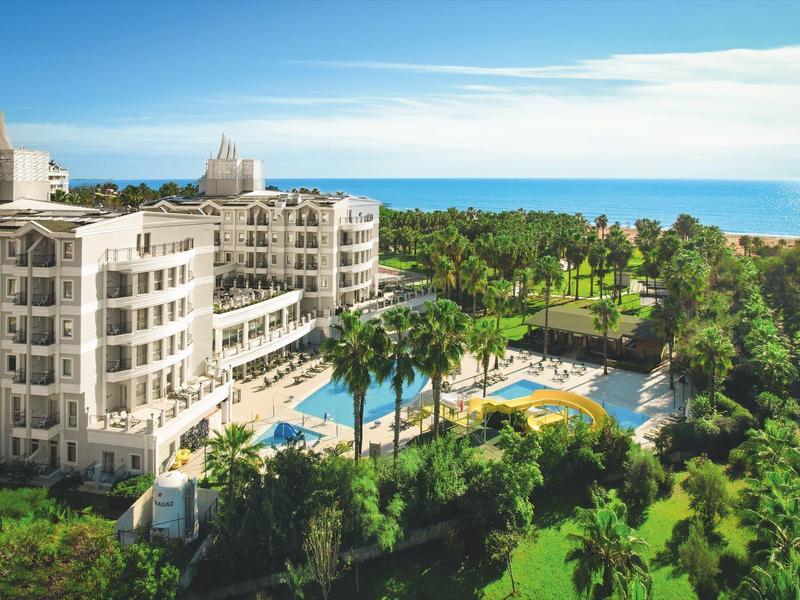Hotel di lusso con piscina, palme e vista sul mare blu sotto un cielo limpido.