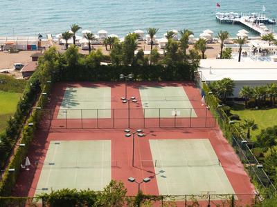 Quattro campi da tennis con superfici rosse e verdi, circondati da palme vicino alla spiaggia.