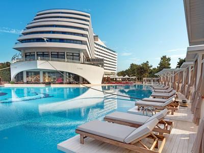 Hotel moderno con piscina all'aperto e lettini sotto ombrelloni in una giornata di sole.