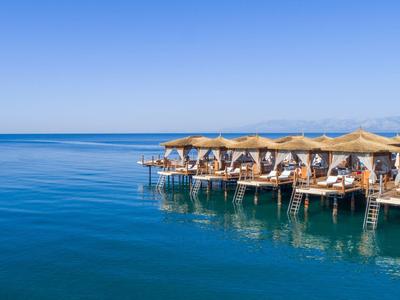 Ombrelloni e lettini su un pontile sopra un mare calmo e blu sotto un cielo terso