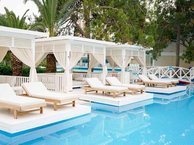 Lettini di lusso e gazebo bianchi accanto a una piscina azzurra in un ambiente tropicale.