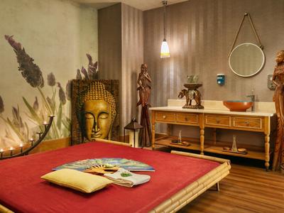 Sala spa con lettino da massaggio rosso, testa di Buddha, sculture in legno e mobile lavabo.