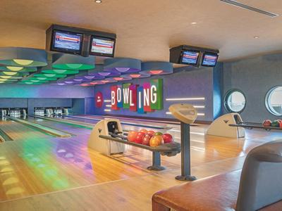 Moderna pista da bowling con illuminazione multicolore, area salotto e diverse corsie.