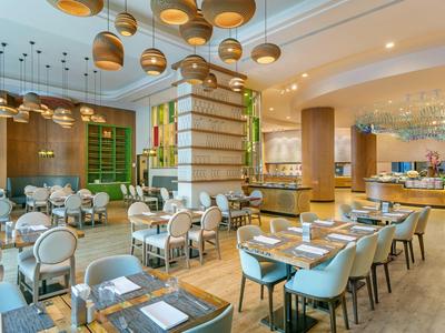 Interno moderno di ristorante con eleganti sedie bianche, tavoli in legno e lampade sospese di design.