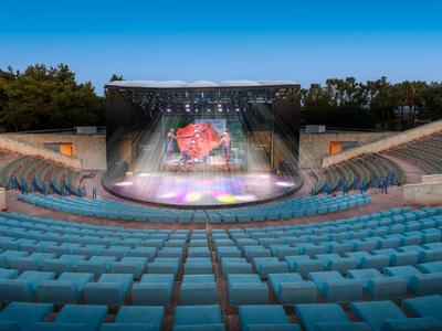Anfiteatro vuoto con sedili blu e palco illuminato al crepuscolo.