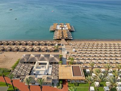 Zona spiaggia con lettini, ombrelloni e bungalow su palafitte sull'acqua.