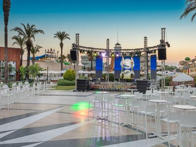 Area esterna vuota con sedie bianche e palco, pronta per un evento al tramonto.