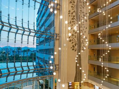 Atrio di hotel moderno con luci pendenti e soffitto di vetro con vista sulla città.