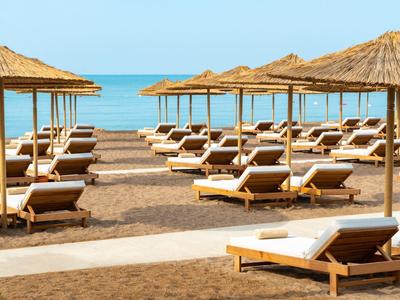 Lettini con cuscini bianchi sotto ombrelloni di paglia su una spiaggia sabbiosa vicino al mare.
