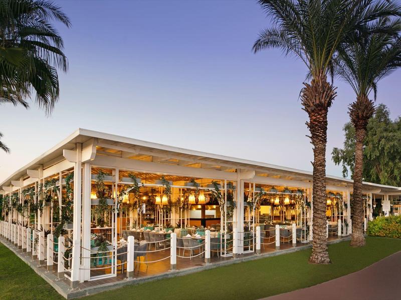 Area pranzo all'aperto circondata da palme sotto un cielo limpido.