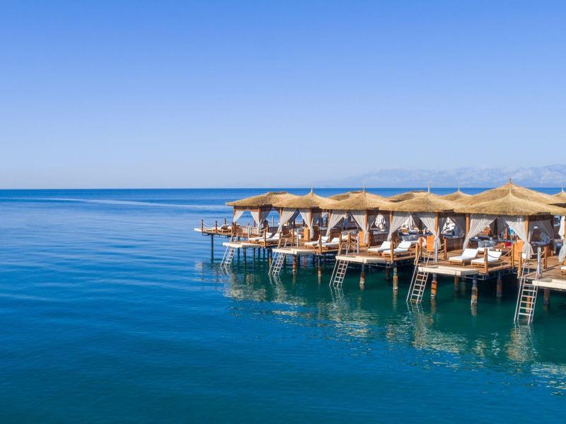 Ombrelloni e lettini su un pontile sopra un mare calmo e blu sotto un cielo terso