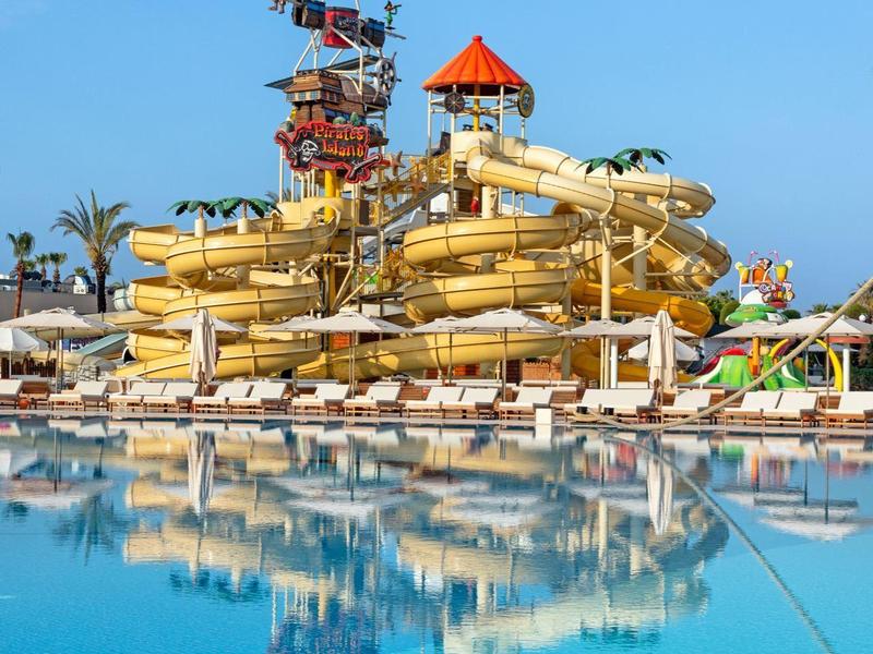 Grande complesso di scivoli gialli su una piscina scintillante sotto un cielo blu chiaro.