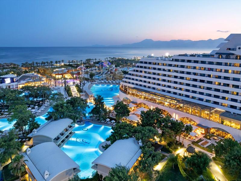 Grande resort con più piscine e palme vicino al mare al tramonto.
