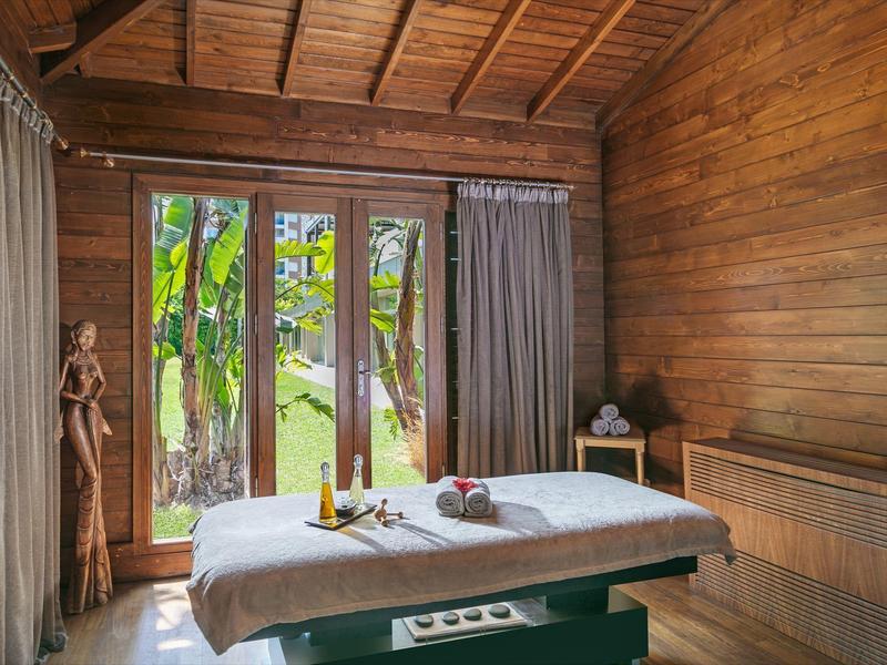 Accogliente stanza spa in legno con lettino da massaggio e grande finestra con piante verdi fuori.