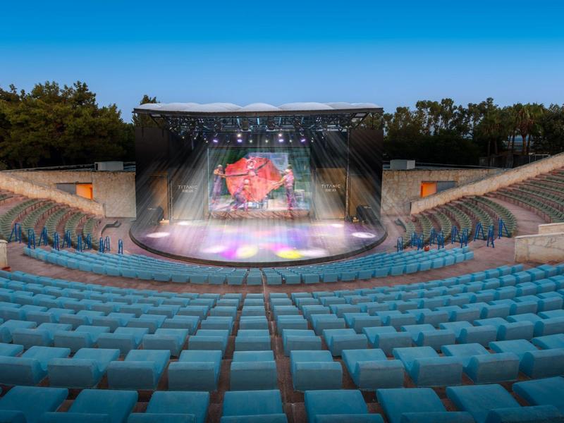 Anfiteatro all'aperto con sedili blu e un grande palcoscenico con effetti di luce al crepuscolo
