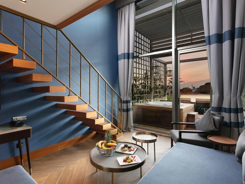 Soggiorno moderno con pareti blu, scale in legno e balcone al tramonto.