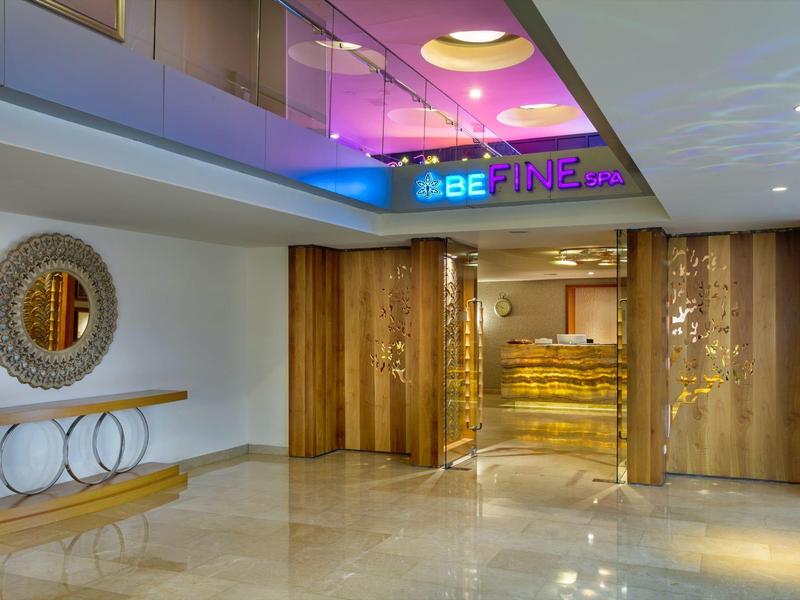 Lobby di hotel moderno con specchio circolare, panche di legno e illuminazione calda.