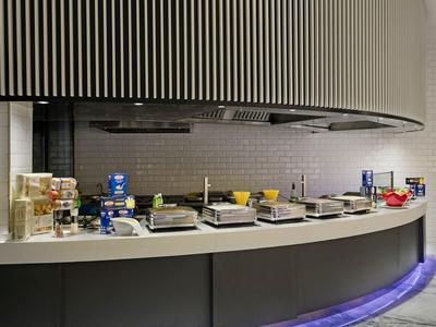 Modern hotel breakfast buffet with cereals, jams, and juice containers on a curved counter.