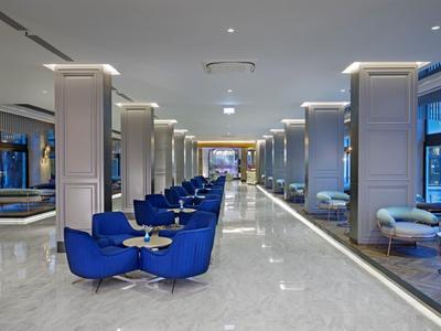 Modern hotel lobby with marble floor, blue chairs, and glass windows.
