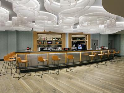Modern hotel bar with stylish stools, illuminated ceiling, and wooden flooring.