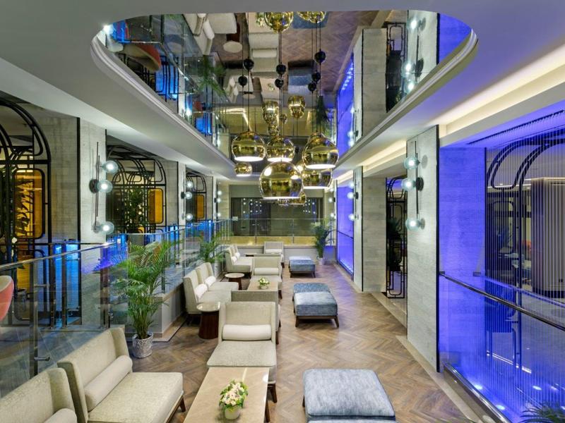 Modern hotel lounge with beige chairs, glass railings, and blue lighting accents.