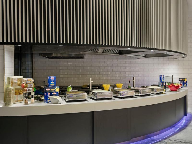 Modern hotel breakfast buffet with cereals, jams, and juice containers on a curved counter.