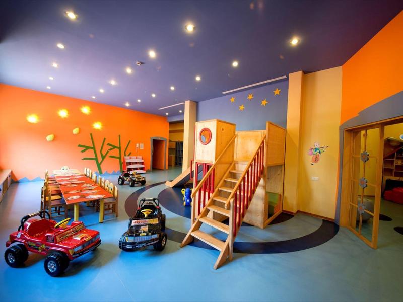 Bright indoor playroom with toy cars, climbing structure, and colorful walls in a hotel area.