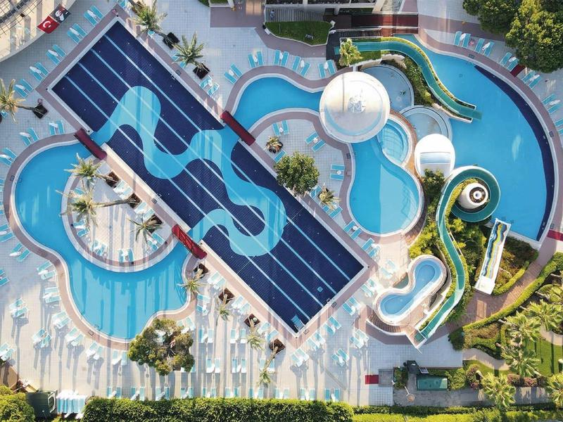 Aerial view of a large outdoor hotel pool area with slides, circular pools, and lounging chairs.