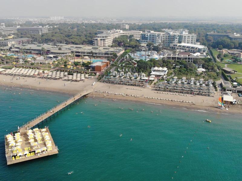 Aerial view of a beach with a pier extending into the sea and buildings in the background.