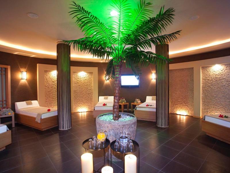 Luxurious spa room with beds, warm lighting, and central palm tree decoration.