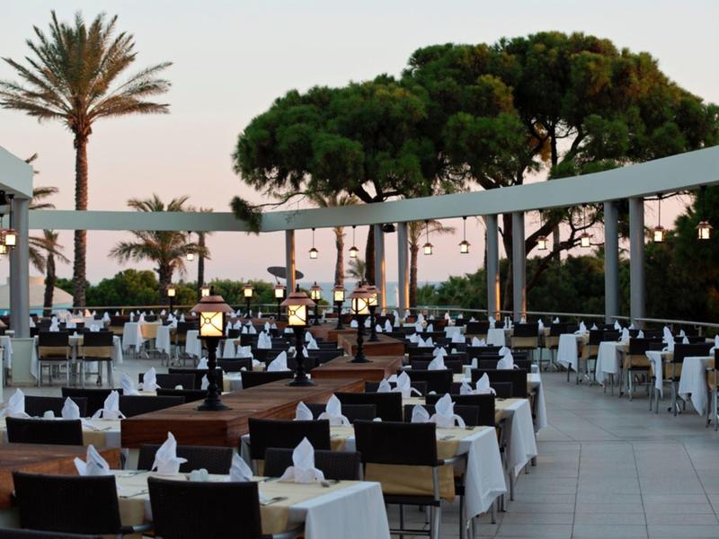 Outdoor restaurant seating with white tablecloths under palm trees at sunset.