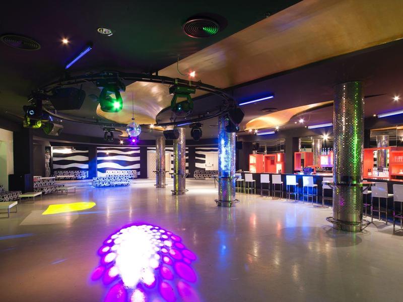 Spacious nightclub with colorful lights, bar counters, and polished floor for dancing.