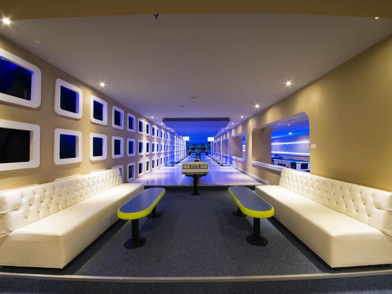 Modern lounge with white sofas, colorful stools and illuminated wall panels in hotel corridor.