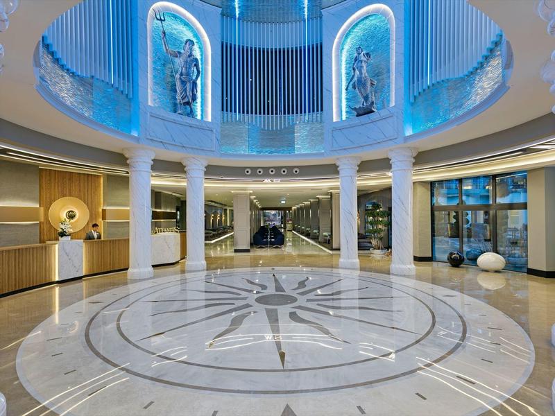 Spacious hotel lobby with circular marble floor, sculptures, and modern lighting.