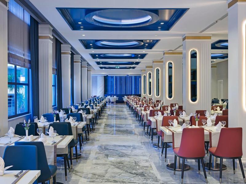 Elegant hotel dining room with marble floor, blue and red chairs, and neatly set tables.
