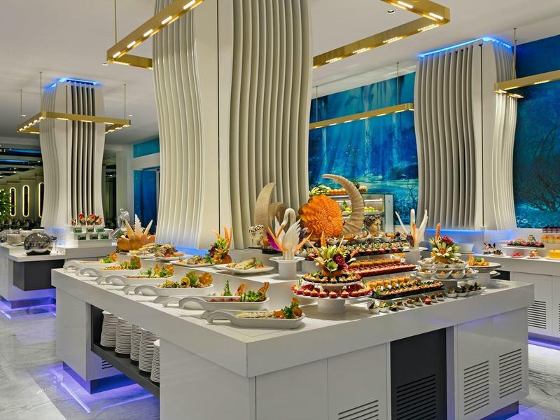 Modern buffet setup in a spacious dining area with elaborate food displays and blue accent lighting.