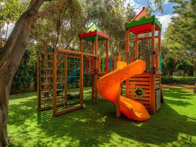Bunter Kinderspielplatz mit Rutsche in einem grünen Hotelgarten unter Bäumen.