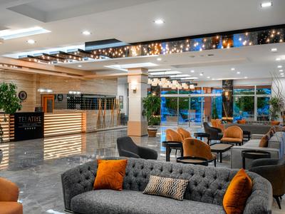Moderne Hotellobby mit grauen und orangenen Sitzmöbeln und einer hell erleuchteten Rezeption.