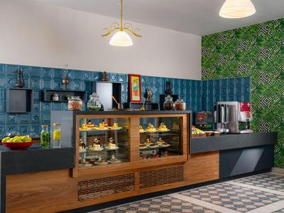 Moderne Hotelküche mit blau gekachelten Wänden, grüner Pflanzenwand und Vitrine mit Gebäck.