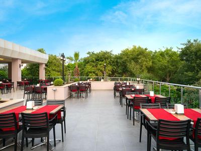 Große Hotelterrasse mit Tischen, Stühlen und Blick auf Bäume unter blauem Himmel.