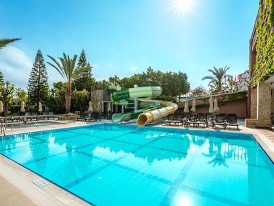 Großer blauer Pool mit Wasserrutsche, Sonnenschirmen und Palmen unter klarem Himmel.
