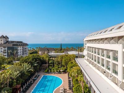 Moderner Hotelkomplex mit Pool, Palmen und Meerblick unter klarem Himmel.