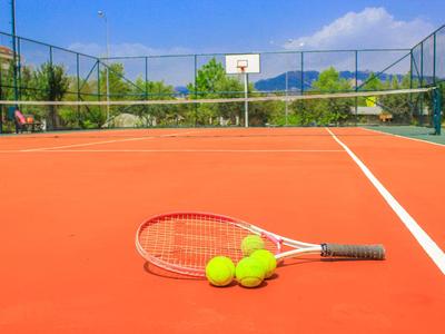 Ein roter Tennisplatz mit Tennisschläger und Bällen vor einem Basketballkorb.