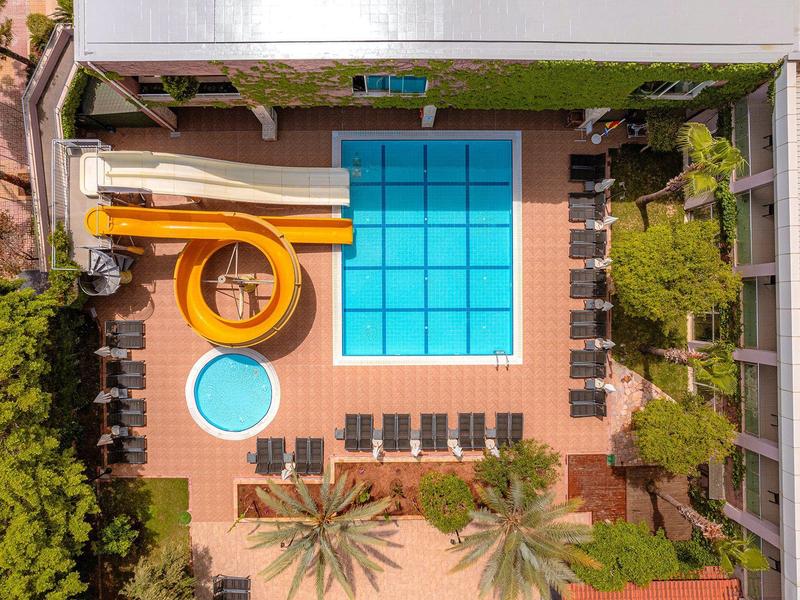 Vue aérienne d'une piscine avec toboggan aquatique et chaises longues dans un jardin d'hôtel.