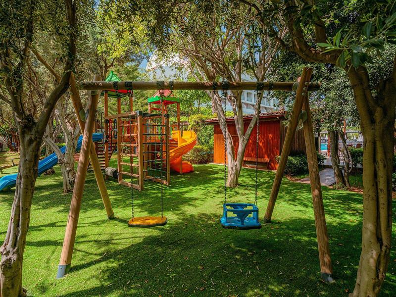 Une aire de jeux avec balançoires et toboggans dans un jardin ombragé.