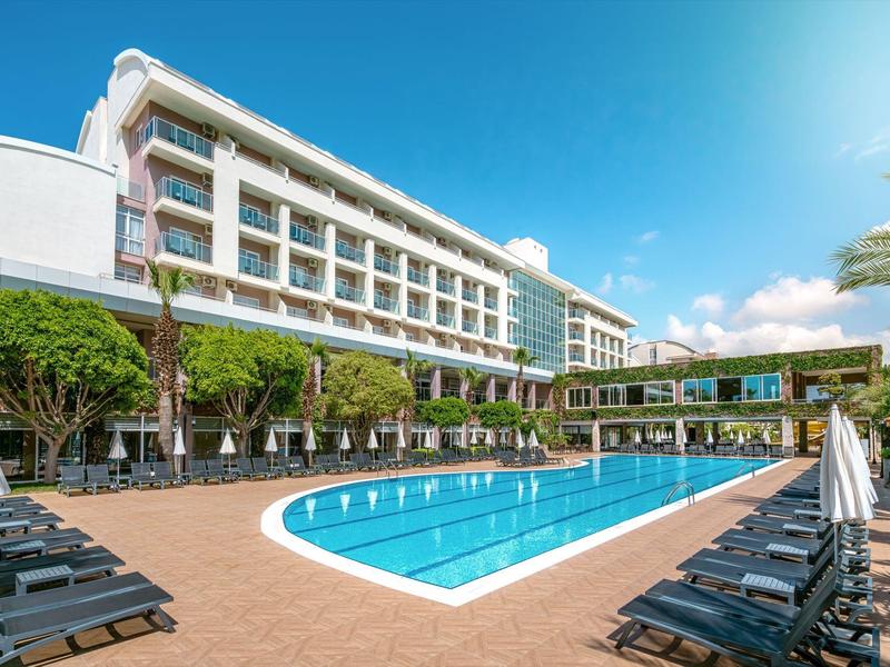 Hôtel moderne avec grande piscine extérieure, chaises longues et ciel dégagé.
