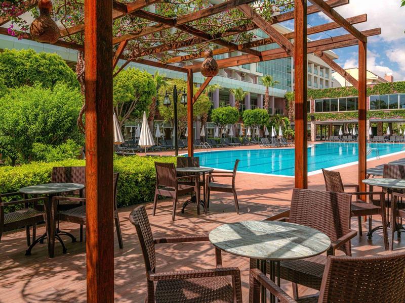 Espace extérieur avec tables et chaises sous une pergola à côté d'une piscine et de végétation verte