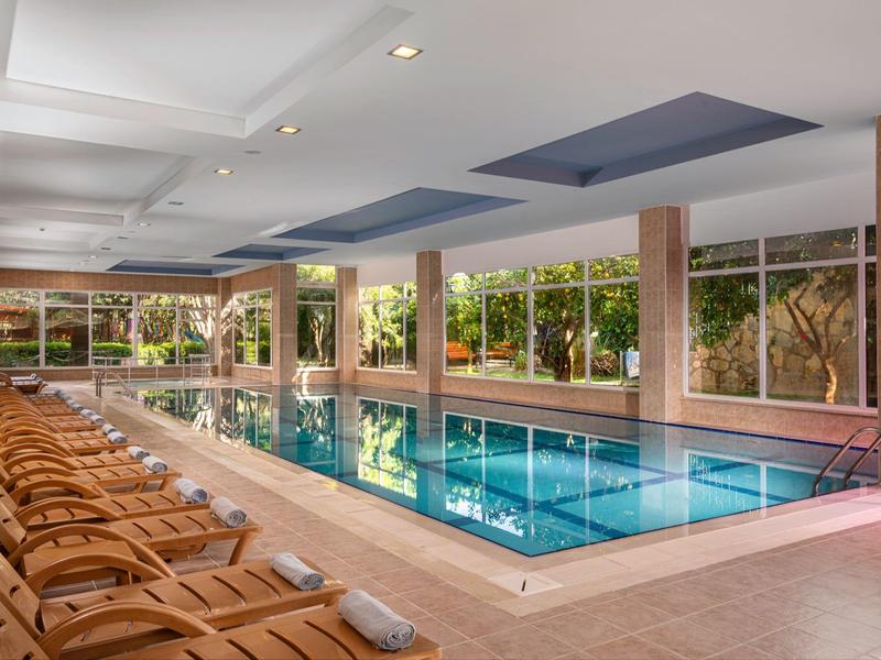 Piscine intérieure avec chaises longues et grandes fenêtres donnant sur le jardin