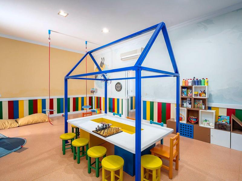 Espace de jeux pour enfants avec petite table, tabourets colorés et étagères dans une pièce lumineuse.
