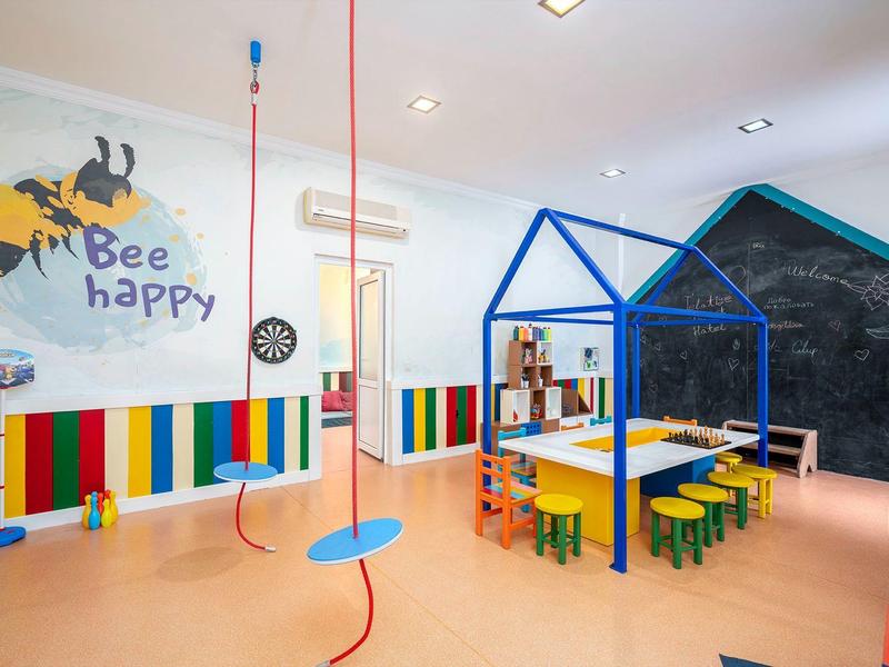 Salle de jeux colorée pour enfants avec tables, petites chaises et balançoires suspendues au plafond.